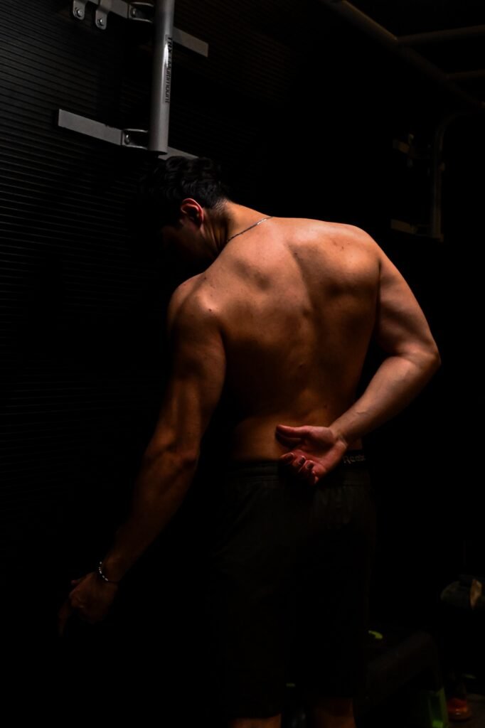 Bodybuilder de dos en contre-jour, relief du dos travaillé, éclairage sombre